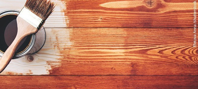 Eine geöffnete Dose Glasur neben einem Pinsel, der auf einer teilweise bemalten Holzoberfläche liegt.